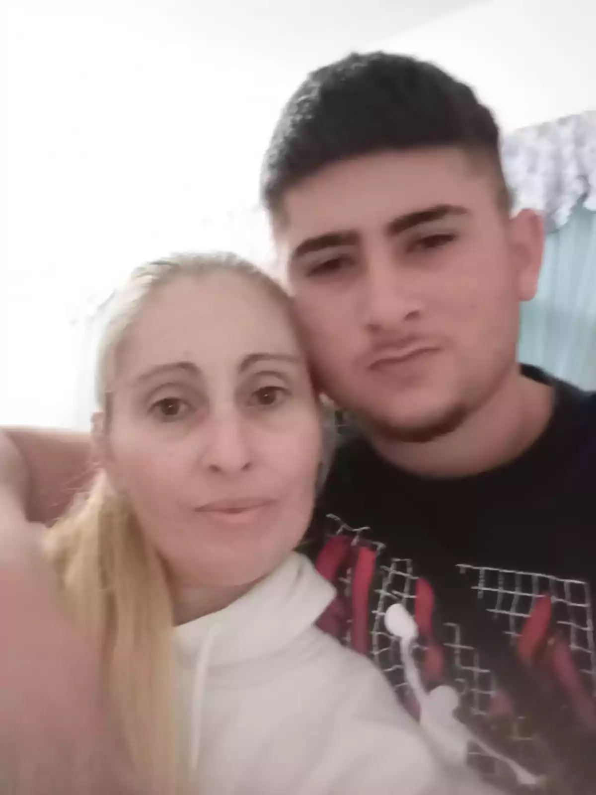 Una mujer y un hombre joven posando juntos para una foto, ambos con expresiones serias.