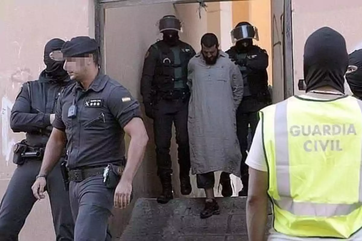 Un grupo de agentes de la Guardia Civil escolta a un hombre esposado mientras lo sacan de un edificio.