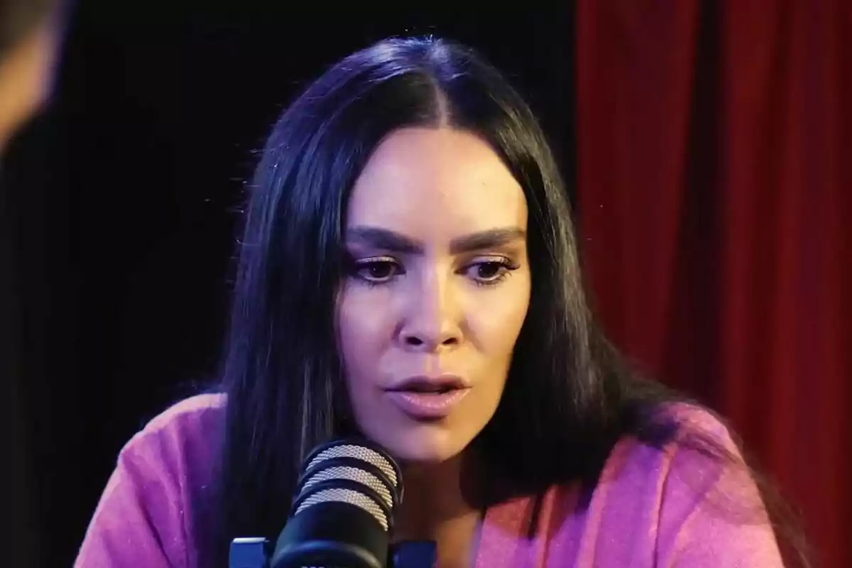 Cristina Pedroche con cabello largo y oscuro hablando frente a un micrófono en un entorno con cortinas rojas.