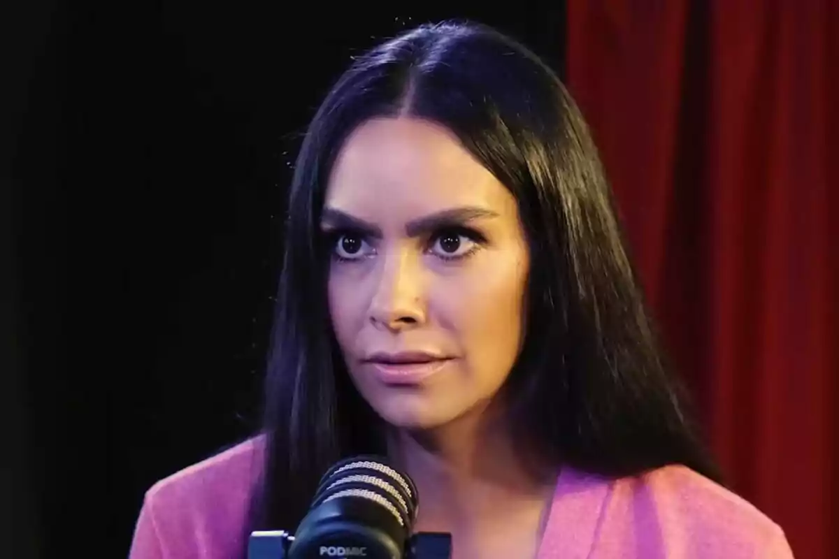 Cristina Pedroche de cabello oscuro frente a un micrófono en un estudio con cortinas rojas de fondo.