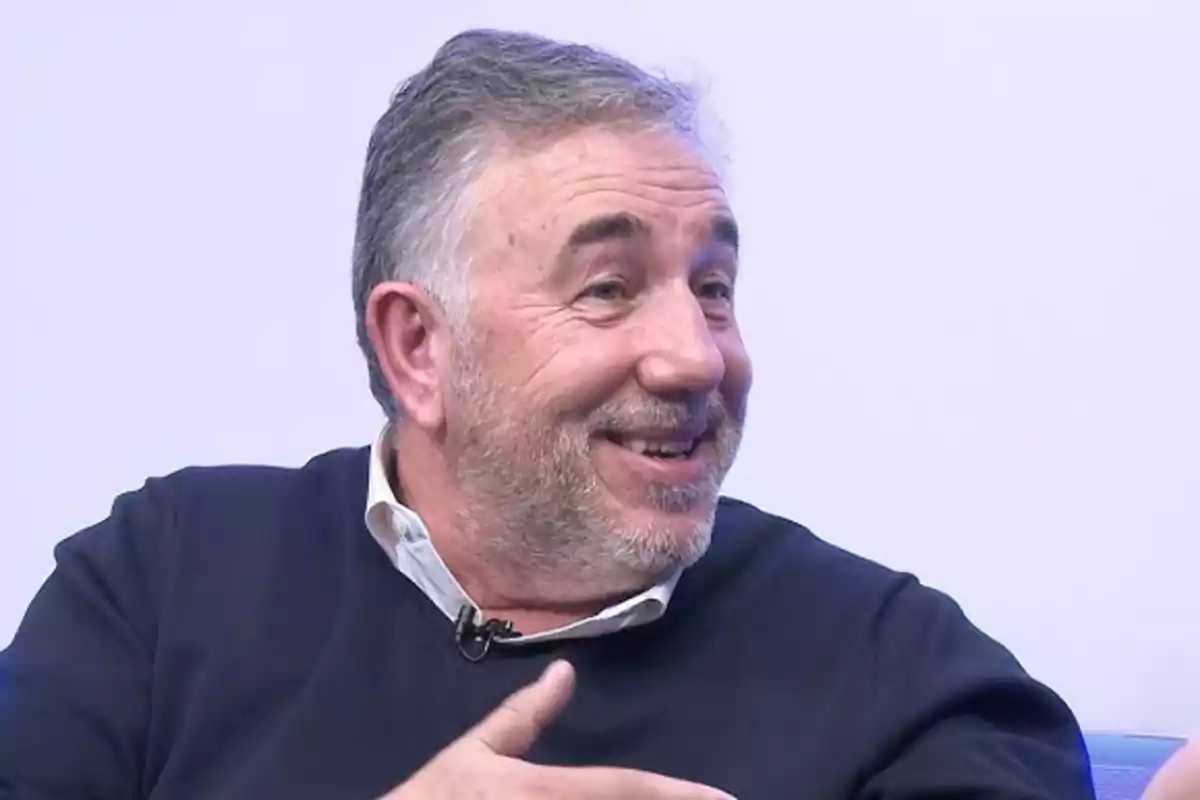Hombre de mediana edad con barba canosa sonriendo y conversando mientras viste un suéter oscuro y camisa clara Hombre de mediana edad con barba canosa sonriendo y conversando mientras viste un suéter oscuro y camisa clara