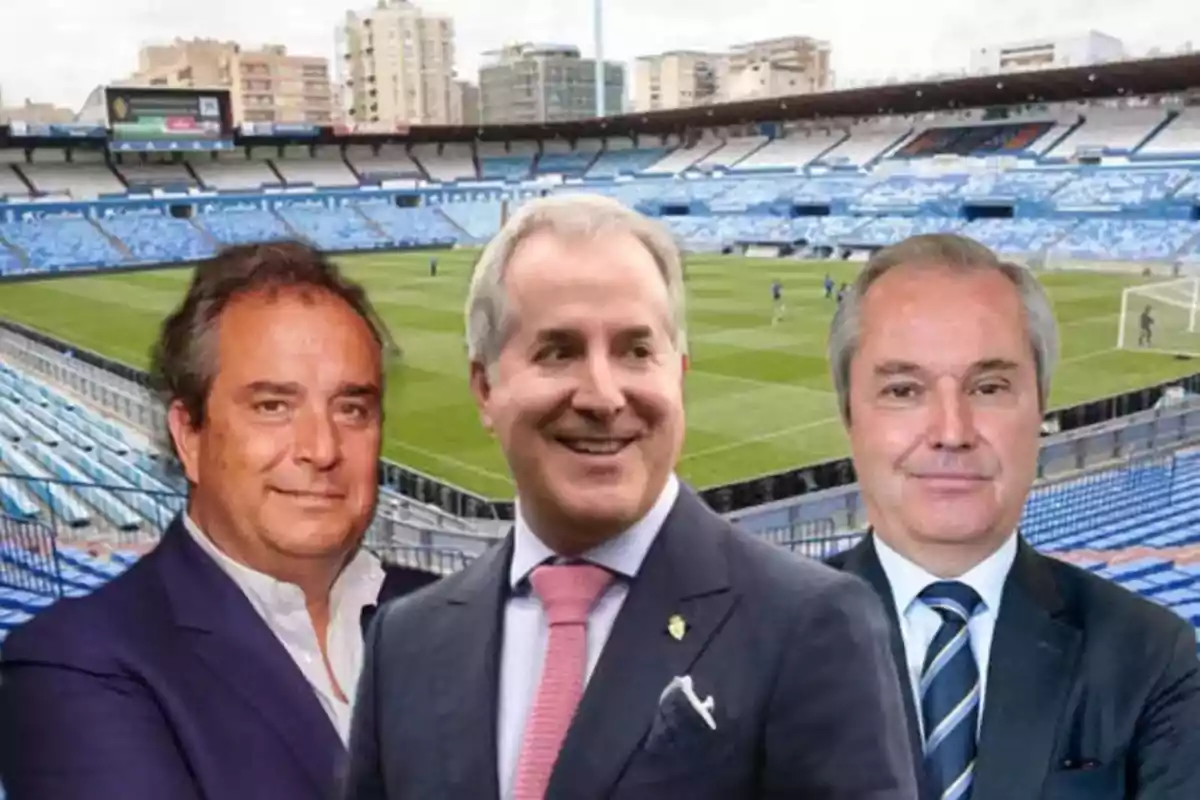 Tres hombres en traje posan frente a un estadio de fútbol vacío.