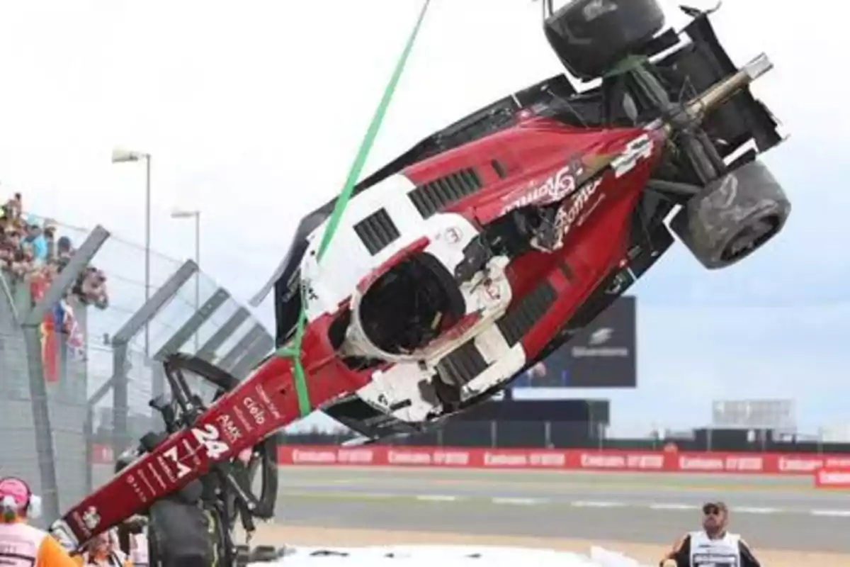 Un coche de carreras volcado siendo levantado por una grúa en un circuito de carreras.