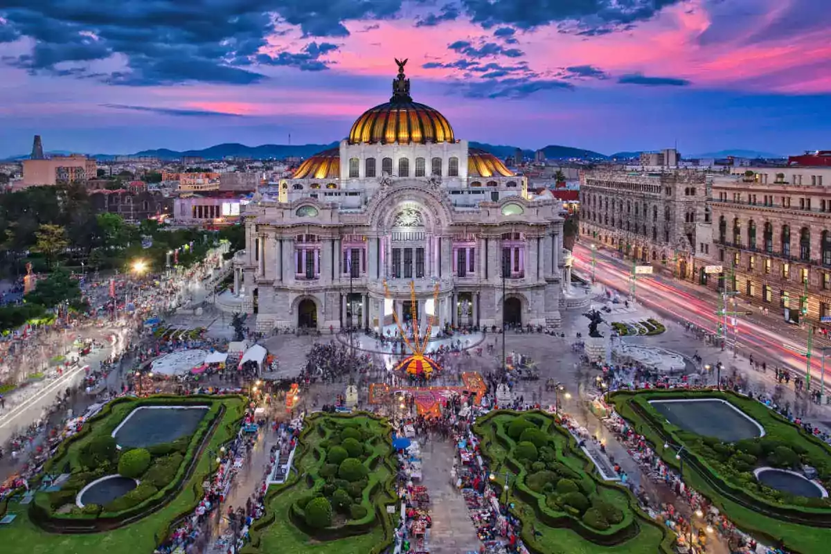 Un edificio histórico con una cúpula dorada al atardecer rodeado de jardines y una multitud de personas.