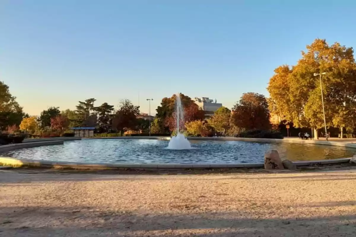 Fuente en un parque rodeada de árboles con hojas otoñales bajo un cielo despejado. Fuente en un parque rodeada de árboles con hojas otoñales bajo un cielo despejado.